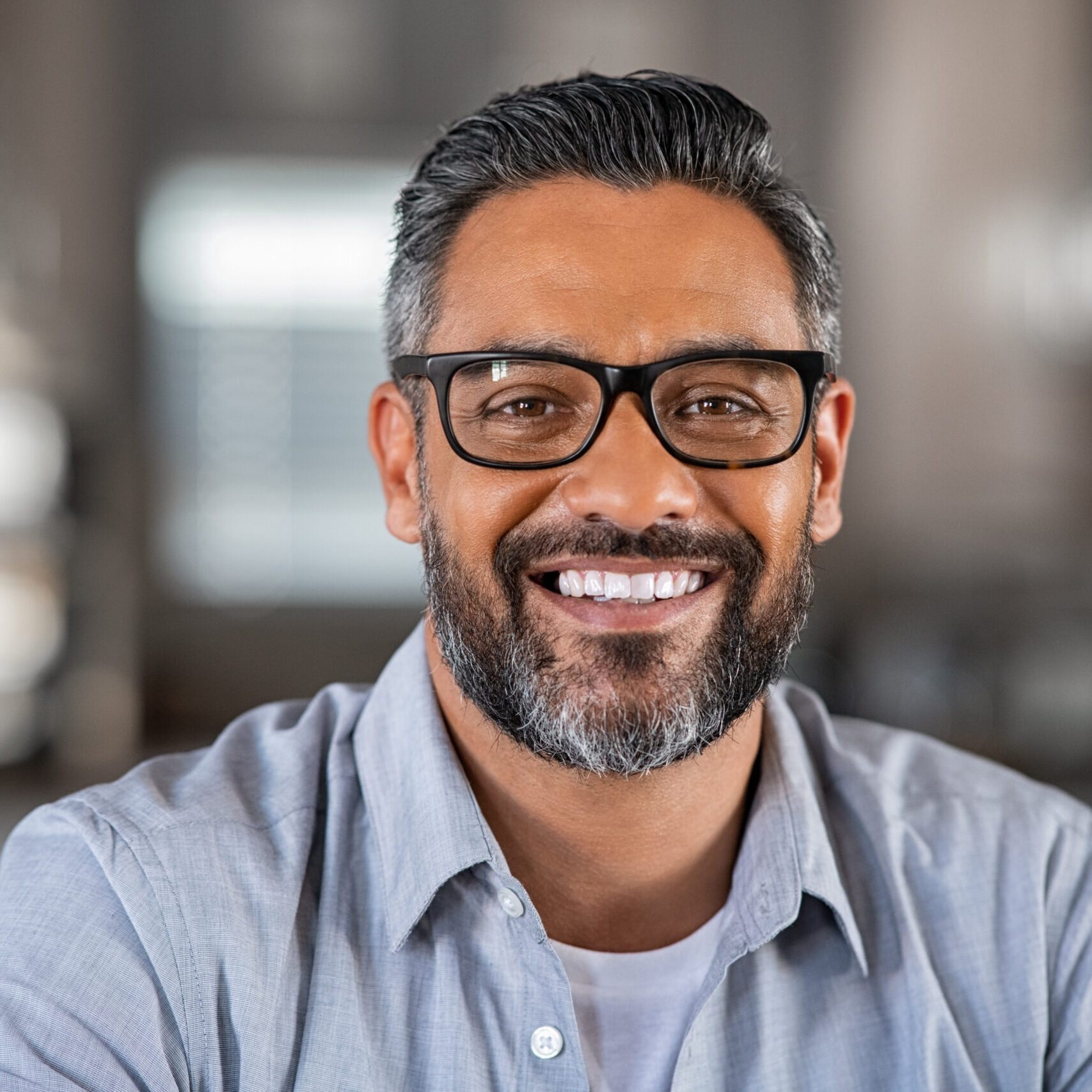 Smiling mature indian man wearing spectacles and looking at camera. Portrait of middle eastern confident businessman at office. Portrait of successful mid entrepreneur feeling satisfied and working from home.