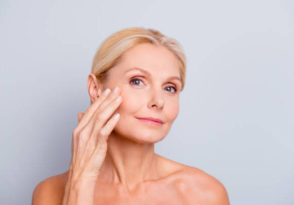 Pretty, charming, attractive woman touching, enjoying her perfect face skin, holding fingers on cheek, pimple, whelk, pustule, dry, oiled, problem skin concept, isolated on grey background